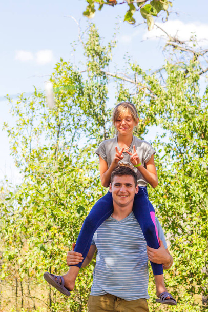 Defocused brother giving sister ride on back. Portrait of happy girl on man shoulders, piggyback. Family playing outside. Summer holidays smiling people concept. Funny horns. Out of focus. - Fotografie, Obrázek