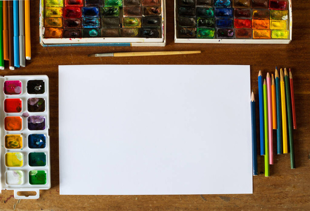 Artist`s table with blank sheet of paper and art tools, flat lay, selective focus, artist`s tools, art supplies, pencils, paintbrush, watercolor paints - Photo, Image