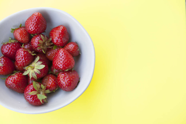 Top view cropped shot of strawberries bowl on yellow background, copy space - Foto, immagini