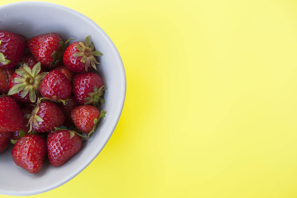 Cropped top view close up of ripe strawberries in a bowl on yellow background - Valokuva, kuva