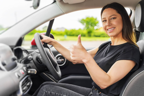 Piękna kobieta w samochodzie pokazuje kciuki do góry. - Zdjęcie, obraz
