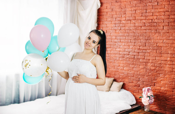 Beautiful pregnant woman is smoothing her tummy and smiling during baby shower. - 写真・画像