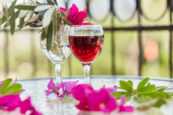 Rosa tropische Blumen und ein Glas Rotwein. Schöne, bunte Sommer Hintergrund. Dekorative rosa Blüten der Bougainvillea in einem Glas. Romantisches Abendessen. Glyphen der Reinigung. Kopierraum - Foto, Bild
