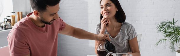 笑顔の若い女性と顔の近くに男がキッチンにコーヒーを注ぐのを見ると - 写真・画像