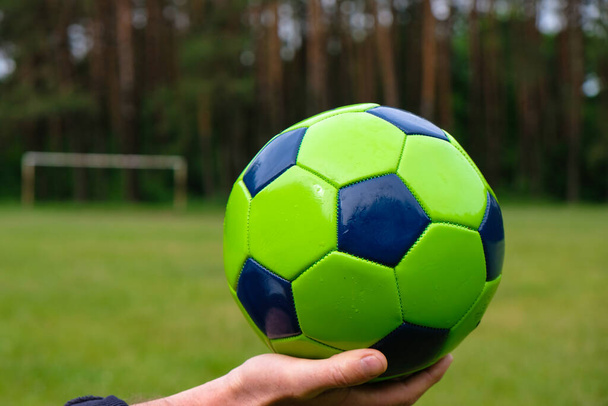 Βρεγμένη μπάλα ποδοσφαίρου στην παλάμη ενός άντρα. Ποδόσφαιρο παιχνίδι σε κάθε έννοια του καιρού. Αντιγραφή χώρου. - Φωτογραφία, εικόνα
