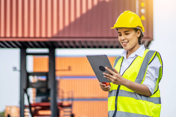 Professional engineer container cargo woman in helmets smiled happily after successfully using the tablet to inspect the stock of export products and information in her business - Foto, imagen