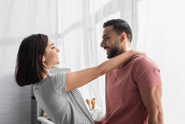 positive young couple looking at each other and hugging in kitchen - Photo, image