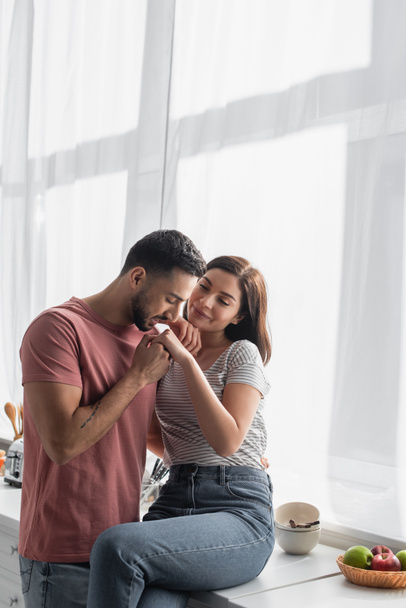 young man with closed eyes kissing hand of girlfriend in kitchen - Foto, imagen
