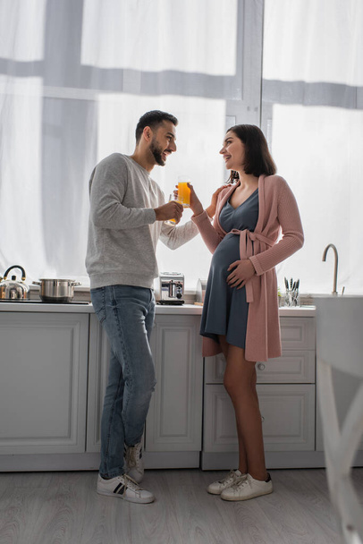 happy young man and pregnant woman standing with orange juice in kitchen - Φωτογραφία, εικόνα