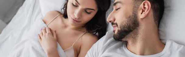 寝室の白いリネンの上で寝ている若い夫婦の高い角度の眺めバナー - 写真・画像