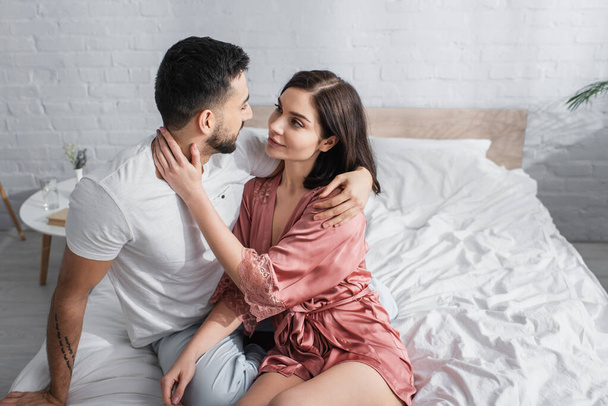 happy young couple gently hugging and looking at each other in bedroom - Фото, изображение