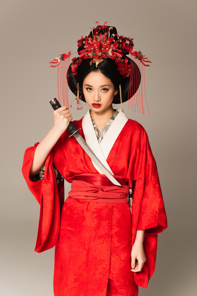 Asian woman holding sword and looking at camera isolated on grey  - Fotografie, Obrázek