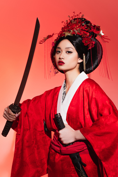 Γιαπωνέζα με ανατολίτικα ρούχα που κρατάει θήκη και σπαθί σε κόκκινο φόντο  - Φωτογραφία, εικόνα