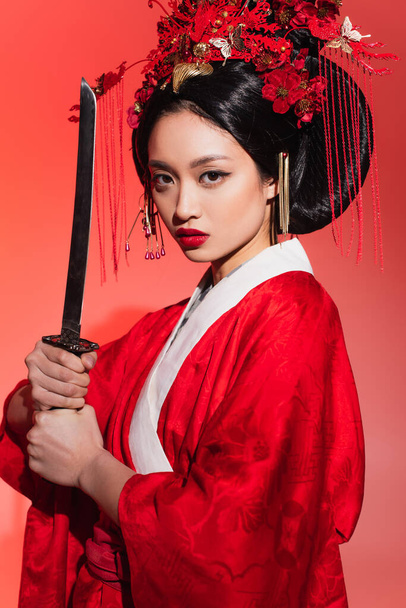 Asian woman in traditional kimono holding sword on red background  - Фото, зображення