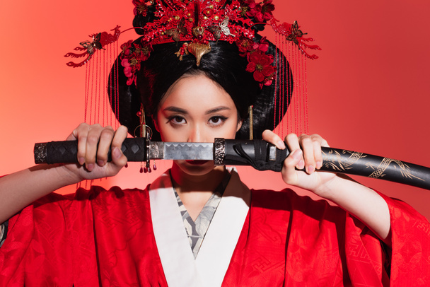 Young asian woman covering face with sword on red background  - Photo, Image