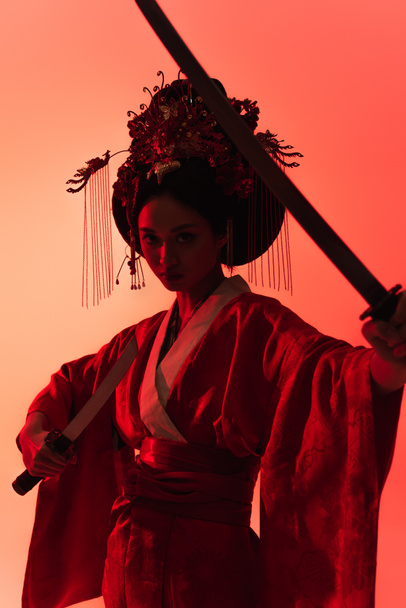 Asian woman with swords looking at camera on red background  - Fotoğraf, Görsel