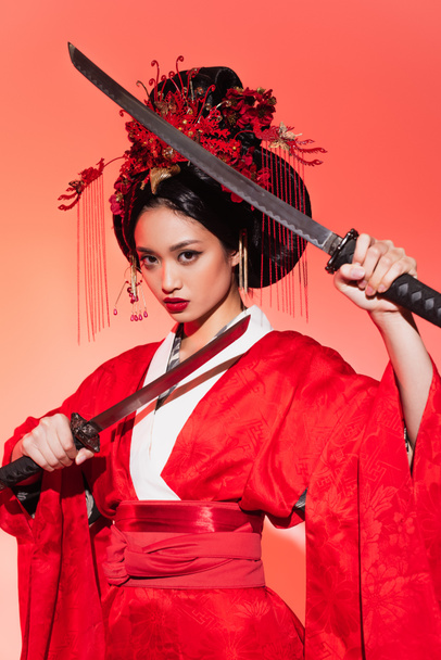 Japanese woman in traditional kimono and hairdo holding swords on red background  - Fotografie, Obrázek