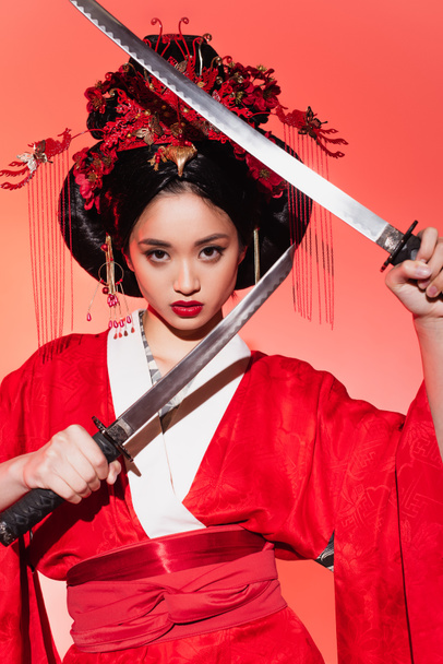 Pretty asian woman in oriental clothes holding swords on red background  - Fotoğraf, Görsel
