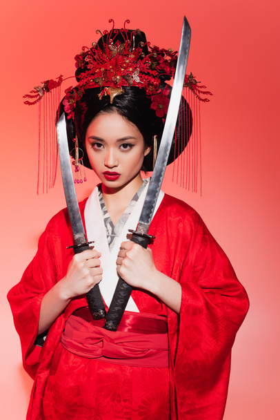 Ιαπωνική γυναίκα με παραδοσιακή ενδυμασία κρατώντας σπαθιά σε κόκκινο φόντο  - Φωτογραφία, εικόνα