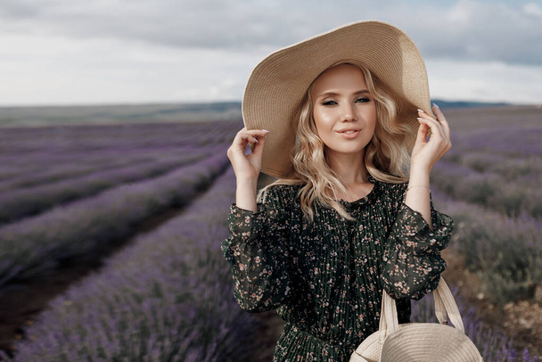 Fashion portrait of a pretty young woman in lavender field in hat with bag - Φωτογραφία, εικόνα