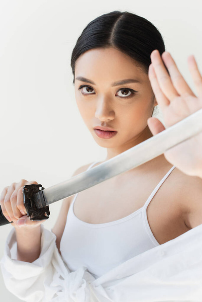 Young japanese woman touching sword on blurred foreground isolated on grey - Fotoğraf, Görsel