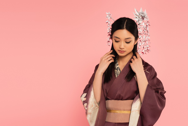 Giovane donna asiatica in kimono regolazione bruna capelli isolati su rosa  - Foto, immagini