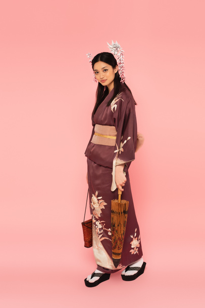 Asian woman with handbag and umbrella standing on pink background - Foto, Imagem