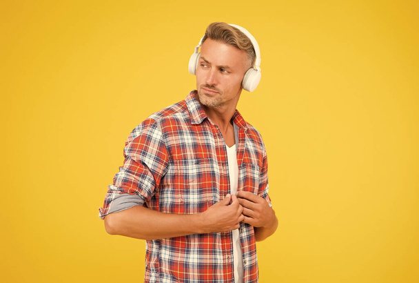 Handsome man button casual shirt listening to music in modern headphones yellow background, modern life - Фото, изображение