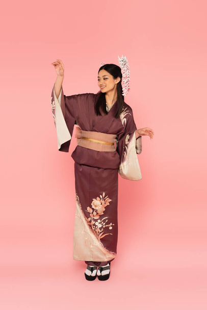 Full length of positive asian woman in oriental wear posing on pink background - 写真・画像