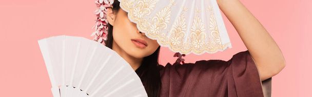 Young woman holding oriental fans near face isolated on pink, banner  - Foto, imagen