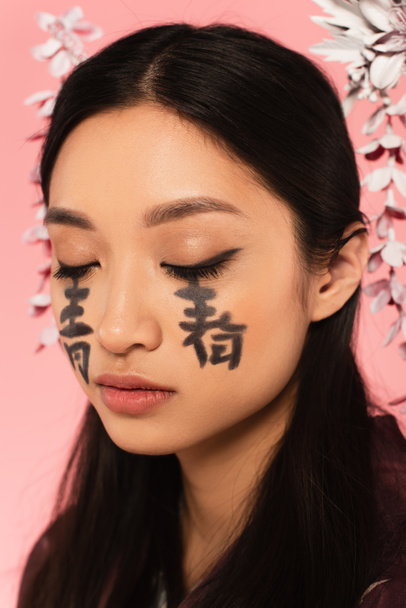 Asian woman with closed eyes and hieroglyphs on face isolated on pink  - Fotoğraf, Görsel