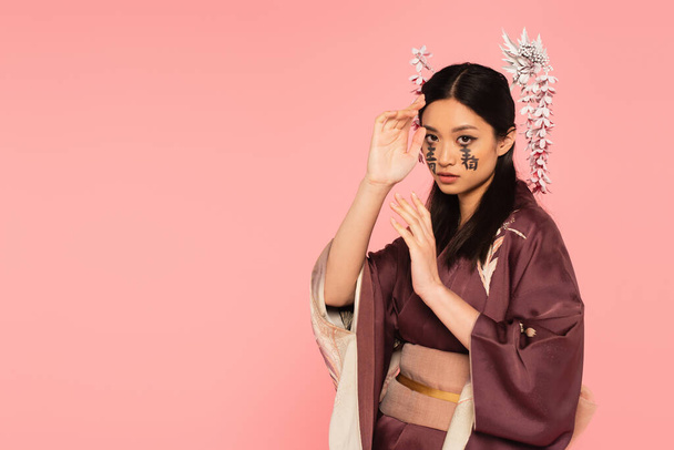 Young asian woman with hieroglyphs on face posing isolated on pink  - Foto, imagen