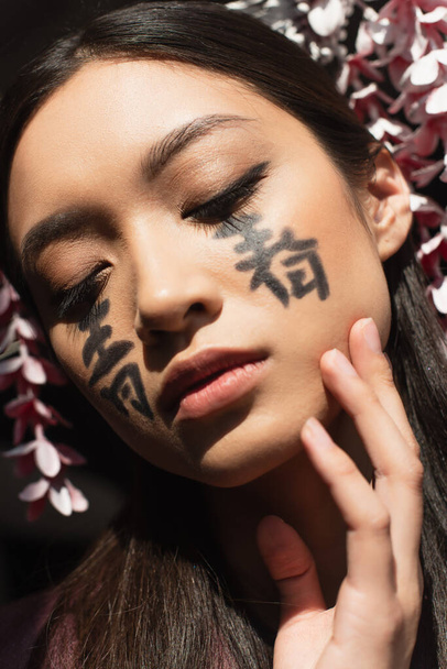 Portrait of asian woman with hieroglyphs on face and kanzashi isolated on black  - Foto, immagini
