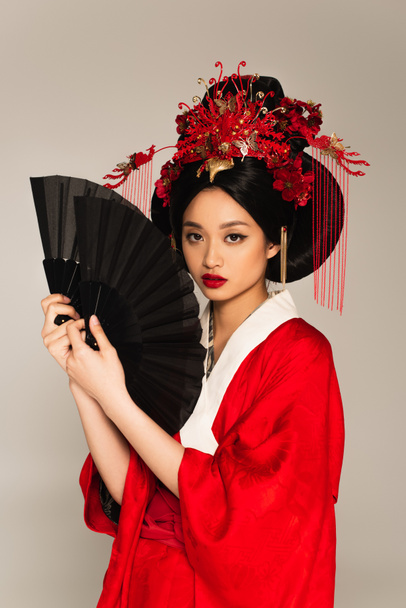 Hezké asijské žena v červené kimono držení ventilátory a při pohledu na kameru izolované na šedé  - Fotografie, Obrázek