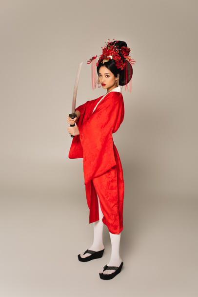 Full length of asian woman holding sword on grey background  - Фото, изображение