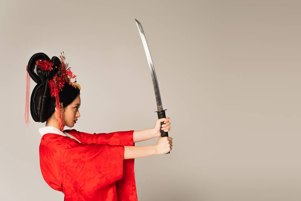 Side view of japanese woman with sword standing isolated on grey  - Foto, imagen