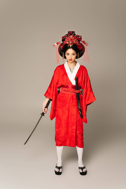 Full length of japanese woman in kimono holding sword on grey background  - Fotografie, Obrázek