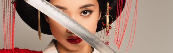 Asian woman covering face with blade of sword isolated on grey, banner  - Fotó, kép