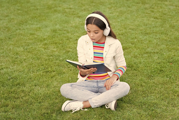 Great Place To Be. new technology in digital life. knowledge day. future school education. teen girl with book on green grass. pretty child little girl read book. study literature for children - 写真・画像