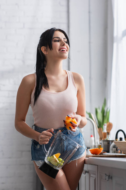 young happy woman holding sliced orange and blender jug  - Foto, imagen