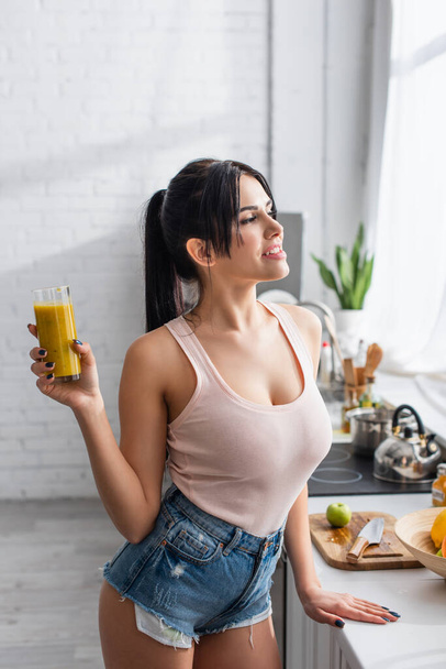 happy young woman holding glass of smoothie in kitchen  - Photo, Image