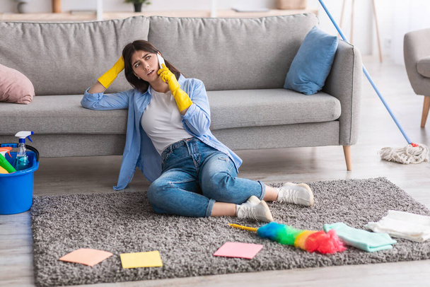 Zmęczona kobieta rozmawiająca przez telefon podczas sprzątania - Zdjęcie, obraz