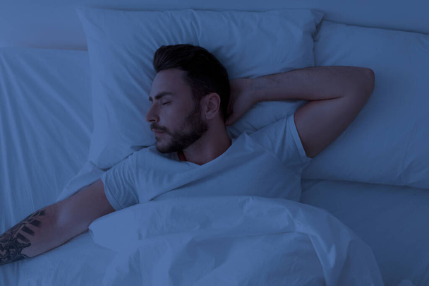 Genç adam geceleri huzurlu bir şekilde uyuyor. Yatak odasındaki rahat yatakta gözleri kapalı yatıyor.. - Fotoğraf, Görsel