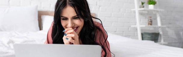 весела молода жінка з зіпсованими руками дивиться на ноутбук у спальні, банер
 - Фото, зображення