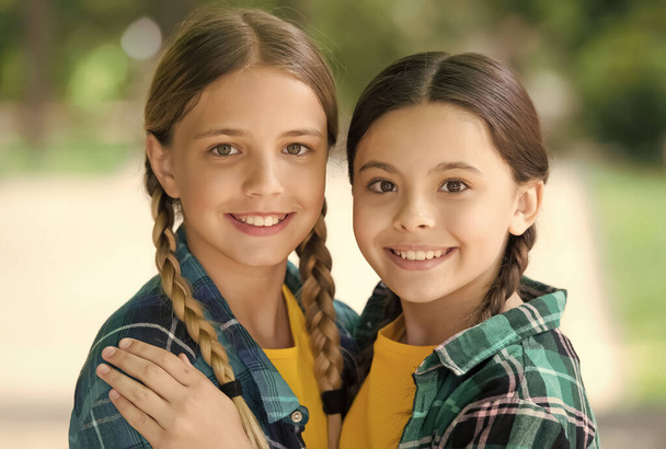 love each other. Two young smiling hipster girls in trendy summer clothes. carefree kids posing outdoor. Positive models. Casual hipsters outfit. portrait of happy sisters. little kids girls in shirt - Fotó, kép