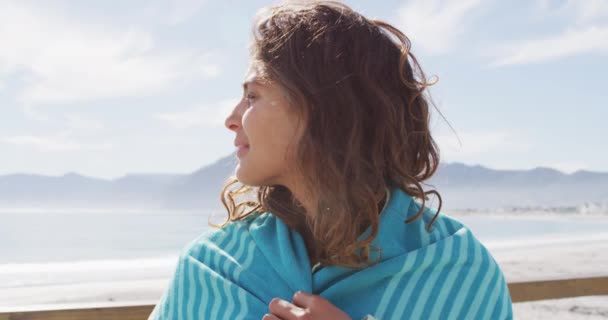 Muotokuva onnellinen sekarotuinen nainen seisoo meren rannalla huopa olkapäiden yli hymyillen. terveellistä elämää, verkon ulkopuolella ja lähellä luontoa. - Materiaali, video