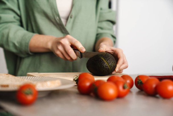 Caucasian woman making salad with avocado at home kitchen - Foto, Imagem
