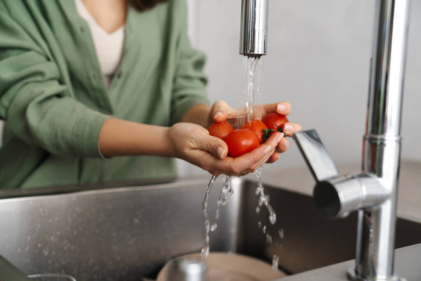 Caucasian young woman washing tomatoes at home kitchen - Valokuva, kuva