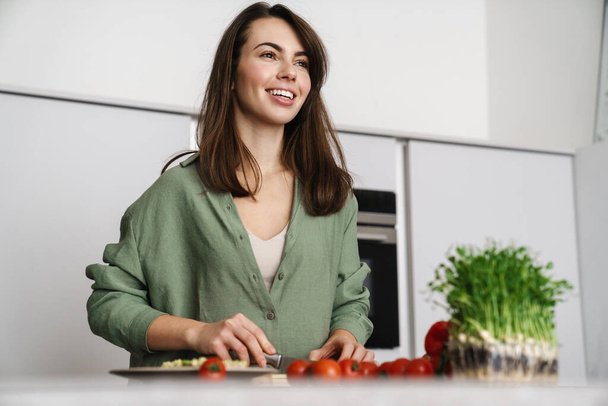 Happy beautiful woman smiling while making salad at home kitchen - Fotografie, Obrázek