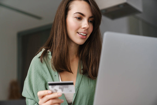 Evde dizüstü bilgisayarla çalışırken kredi kartı kullanan hoş bir kadın. - Fotoğraf, Görsel
